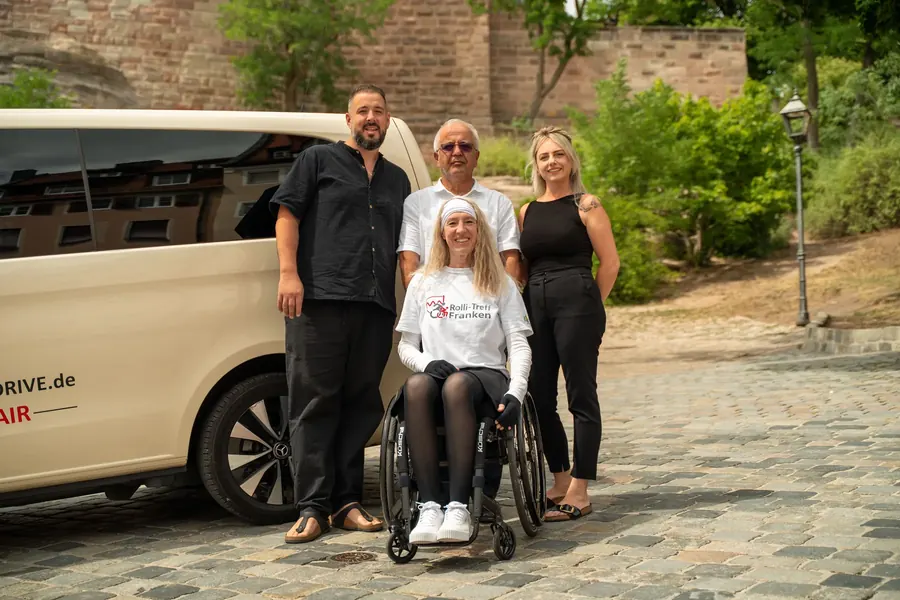 Das Handicap-Drive-Team gemeinsam mit einer Rollstuhlfahrerin vor dem Fahrzeug