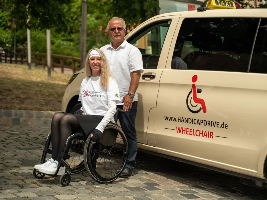 Fahrer begleitet eine Rollstuhlfahrerin am Handicap-Drive-Fahrzeug