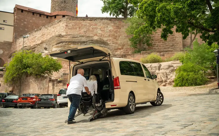 Rollstuhlfahrerin wird über die Rampe in ein Handicap-Drive-Fahrzeug vor der Nürnberger Burg begleitet