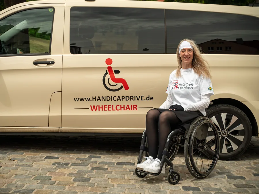 Fahrgastin im Rollstuhl neben dem Handicap-Drive-Taxi