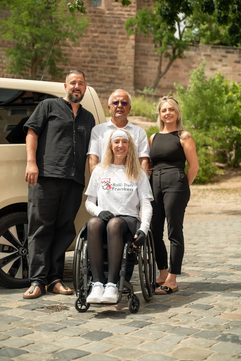 Das Handicap-Drive-Team mit Fahrgastin im Rollstuhl am Fahrzeug