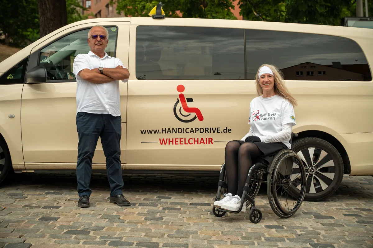 Fahrer und Rollstuhlfahrerin vor einem Handicap-Drive-Fahrzeug der Flotte